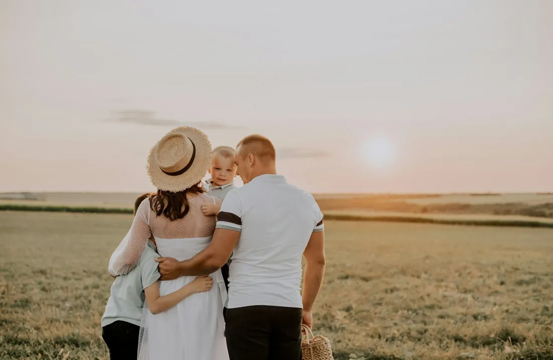 A young family walking through a field at sunset